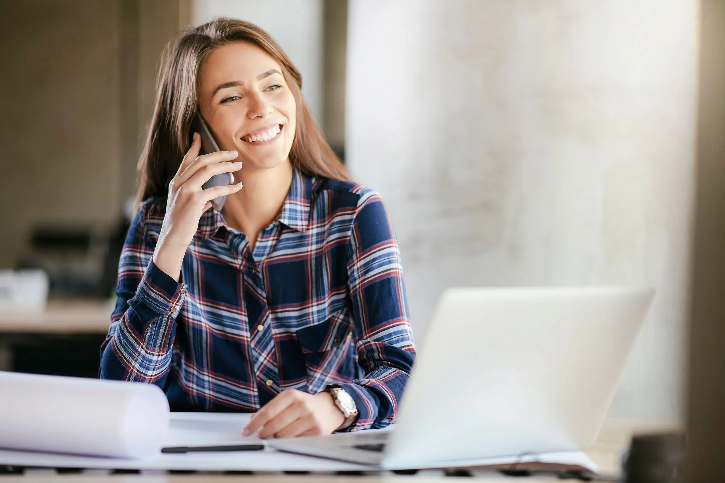 Vrouw belt glimlachend aan haar bureau met een laptop