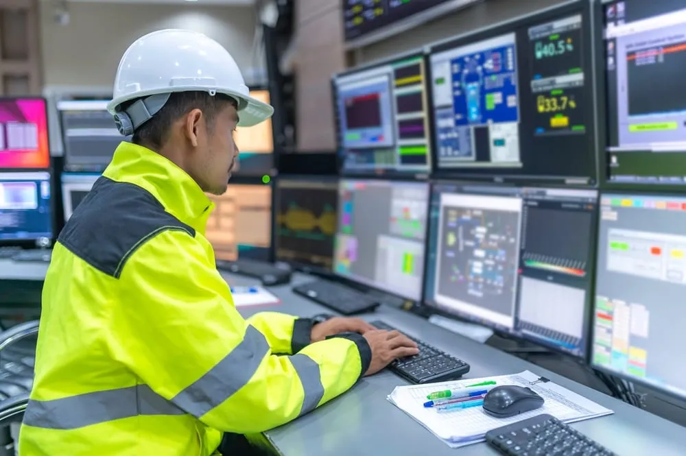 Technicus in werkkleding volgt de opbrengst op beeldschermen in een controlekamer